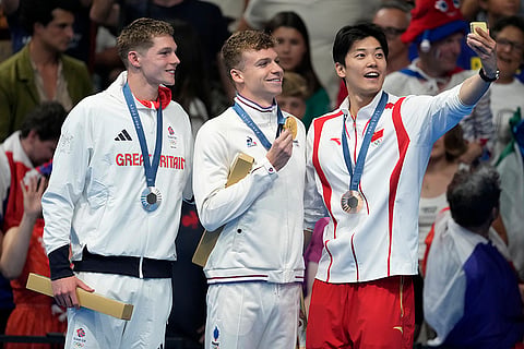 Gold medalist Leon Marchand, centre stands with silver medalist Duncan Scott and bronze medalist Shun Wang 
